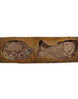 Brown wooden antique Chinese rice mold with carved fish and flower designs, close-up on plain background.