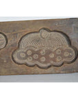 Close-up of antique Chinese rice mold, brown wood with circular top and dotted decorative patterns, on neutral background.