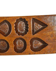 Brown antique Chinese wooden rice mold with six carved floral and geometric designs, close-up on plain background.