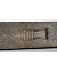 Brown wood Chinese rice mold with coin, fish, and diamond cavities on a weathered surface.