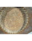 Close-up of a weathered antique Chinese rice mold with a round motif and braided rim on a textured surface.