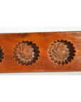 Close-up of antique wooden Chinese rice mold with four rosette cavities and a long handle, on a plain background.