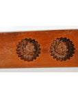 Brown wooden antique Chinese rice mold with four rosette cavities and a long handle, close-up on plain background.