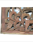 Reddish-brown wood temple carving with intricate floral and leaf designs, close-up.
