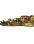 Close-up of a golden intricately carved antique Chinese temple crane sculpture resting on its side against a plain background.