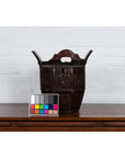 Brown wood Chinese wedding box with carved handle, animal and foliage motifs, on wooden table against white brick wall.