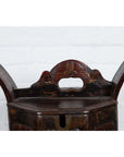 Brown wooden Chinese wedding box with carved handle, animal and foliage motifs, against a white brick wall indoors.