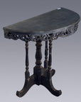 Brown wood antique demi lune table with carved trim and four turned legs, set against a plain gray background.