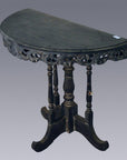Brown wooden antique demi lune table with ornate carved edges and four turned legs, shown against plain background.