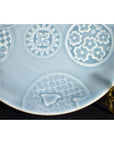 Close-up of a white embossed Chinese porcelain plate with circular floral and geometric patterns.