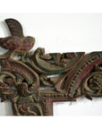 Close-up of an antique hand-carved wooden mirror frame with ornate corners, perched bird, floral motifs, green and red hues.