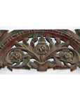 Close-up of antique hand carved wooden mirror frame with intricate floral and leaf designs in dark red and green tones.