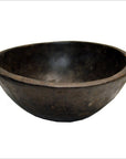 Brown hand-carved wooden bowl with round, shallow shape and uneven rim on white background.