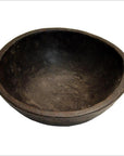 Close-up of rustic dark brown hand carved wooden offering bowl against a plain white background.