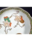 Close-up of white porcelain Asian bowl with red, green, and gold hand-painted floral and leaf patterns.