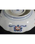 White ceramic bowl base with blue and orange floral motifs and central maker's mark, close-up.