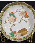 Close-up of an antique hand painted Asian ceramic bowl with floral, green leaf, and orange berry design on metal stand.