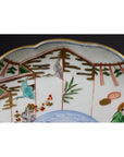 White porcelain plate with hand-painted cranes, green foliage, and geometric fence, scalloped rim, close-up.