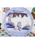 Close-up of blue and white ceramic Asian plate with hand-painted figure, water, trees, grass, and ornate patterns.