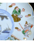 Close-up of antique hand painted Asian ceramic plate with figures in traditional attire holding objects beside barrels.