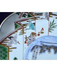 White porcelain plate with hand-painted cranes, green fans, bamboo, and floral accents, close-up view.