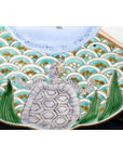 Colorful ceramic plate with turtle and snake design, green leaves, and blue waves on surface.
