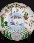 Close-up of a colorful hand painted ceramic Asian plate featuring figures, a turtle, and traditional nature scenes.
