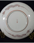 Close-up of the back of an antique hand painted Asian ceramic plate with red patterns on a brass stand.