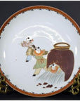 White porcelain Asian plate with hand-painted figures in traditional attire, displayed on a metal stand.