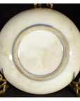 Close-up of antique hand painted Asian plate with blue ring on brass stand against a dark background.