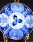 Blue and white hand painted ceramic Asian plate with Chinese characters on brass stand, close-up view.