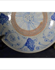 Close-up of blue and white hand painted Chinese porcelain plate with sun face center on brass stand.
