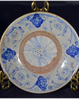 Close-up of antique hand painted ceramic plate with blue floral and swirl designs on a gold stand.