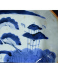 Blue and white porcelain plate with hand painted Chinese landscape, trees, and pagoda design.