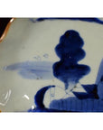 Close-up of blue and white hand-painted antique Chinese porcelain plate with orange rim on dark background.