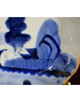 Close-up of blue and white porcelain plate with gold-trimmed wavy edge and hand painted abstract design.