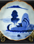 Close-up of blue hand-painted Chinese porcelain plate with brown rim, displayed on a decorative stand.