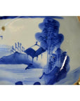 Blue and white porcelain plate with hand-painted Chinese landscape, trees, house, and fence, close-up view.