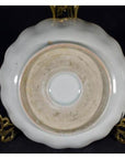 Close-up of an antique hand-painted Chinese porcelain plate with scalloped edge on a brass stand, black background.
