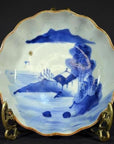 Blue and white hand painted Chinese porcelain plate with landscape design on decorative metal stand.