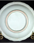 Close-up of antique hand painted embossed Japanese plate with faint pink ring on gold stand against black background.