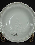 White ceramic Japanese plate with hand painted floral design and black calligraphy, displayed on a stand.