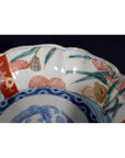 Close-up of blue, red, and green hand painted porcelain Imari bowl with scalloped edge and floral fruit rim motifs.