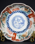 Close-up of an antique Japanese Imari porcelain bowl with red, green, and blue floral patterns on a brass stand.