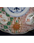 Close-up of antique Japanese Imari porcelain bowl with red, green, and gold hand-painted floral patterns.