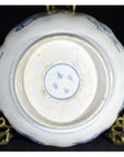 Blue and white porcelain bowl underside with hand-painted designs, shown on a brass stand.