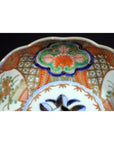 Close-up of antique Japanese Imari porcelain bowl with hand painted intricate red, green, blue, and gold patterns.