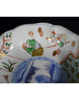 Close-up of antique Japanese Imari porcelain bowl with green and red figures, blue landscape details inside.