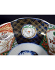 Close-up of antique hand painted Japanese Imari porcelain bowl with intricate red, green, black, and gold rim patterns.