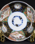 Vibrant multicolor hand painted Japanese Imari porcelain bowl on brass stand against dark background, close-up view.